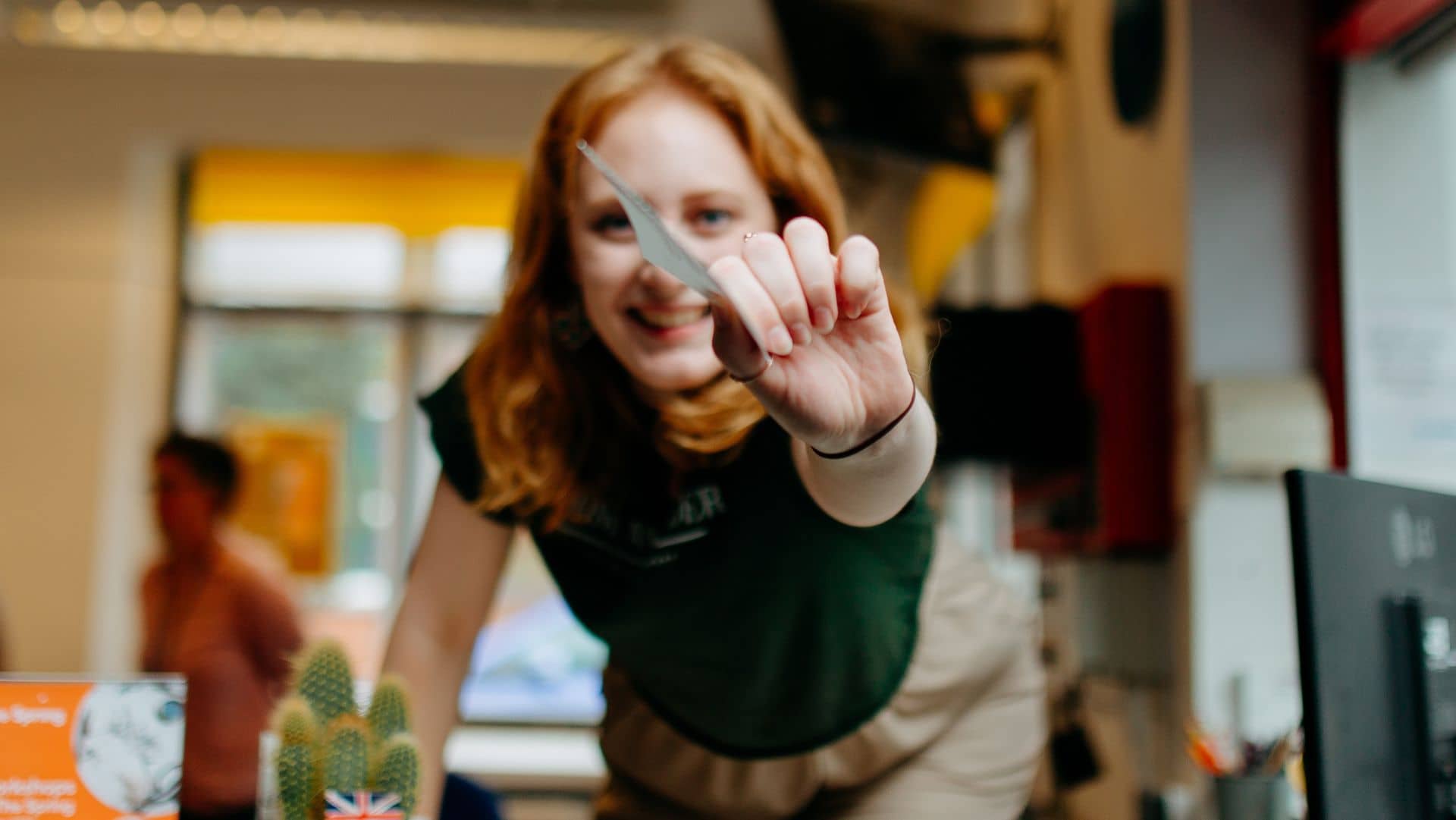 A young girl with ginger leans over the counter of the box office with a paper ticket in her hand as if to hand it to you