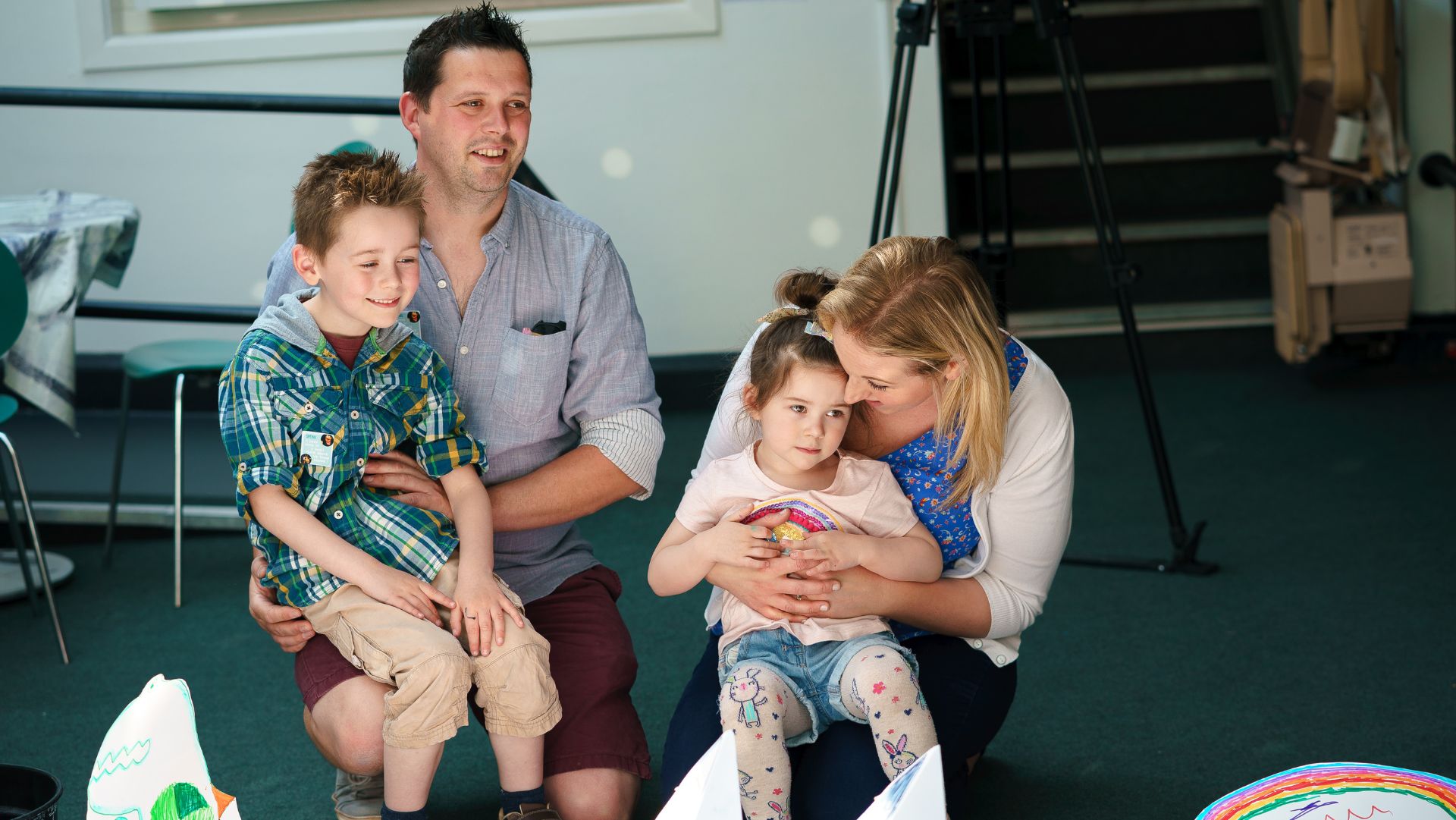 TheSpring_Donate_a family of four sat within our foyer space. The father with dark hair has his son on his lap. The mother has her daughter sat on her lap. They all have happy smiley faces