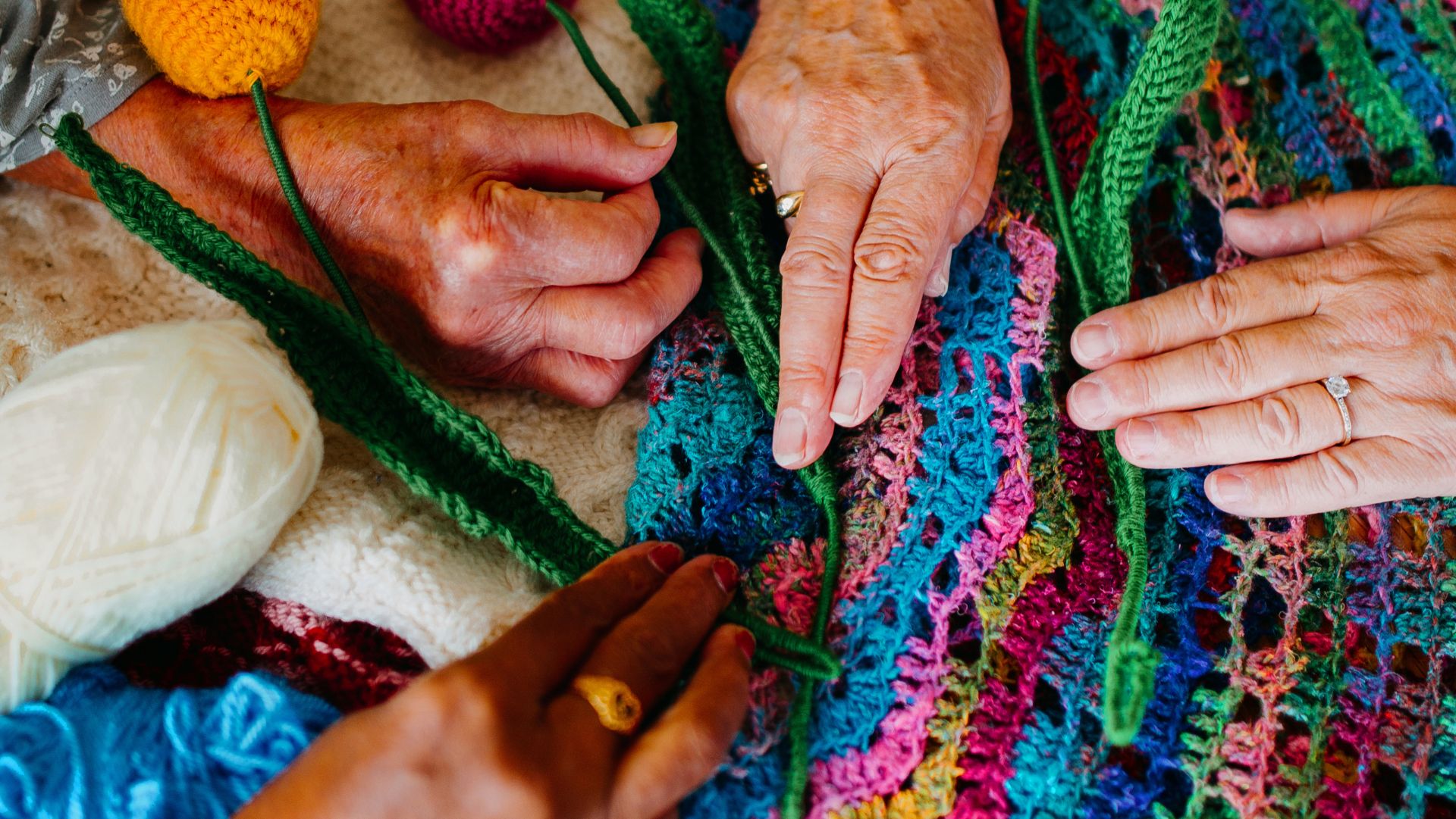 TheSpring_Donate_four hands of elderly women on top of a colourful knitted garment with balls of yarn surrounding them