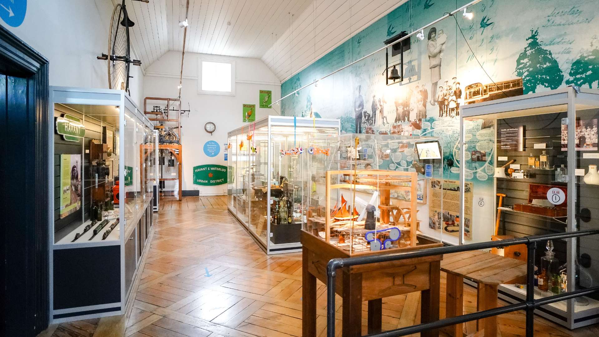 A light museum type room with a wooden floor and white walls. The room includes many artefacts that span the history of Havant.